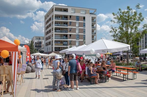 Bei strahlendem Sonnenschein konnten die Besucherinnen und Besucher Livemusik und kulinarische Leckerbissen genießen. (Foto: Buck) Menschen sitzen auf Bierbänken unter Sonnenschirmen, im Hintergrund ein Wohnhaus. (Foto: Buck)