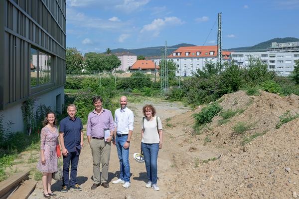 Im Hintergrund wird künftig die neue Gneisenaubrücke verlaufen, die mit dem Rad und zu Fuß überquert werden kann: Erster Bürgermeister Jürgen Odszuck (Mitte) besichtigt mit Mitarbeitenden die künftige Baustelle. (Foto: Philipp Rothe)