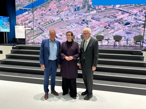 Drei Menschen stehen vor einer modernen Bühne.