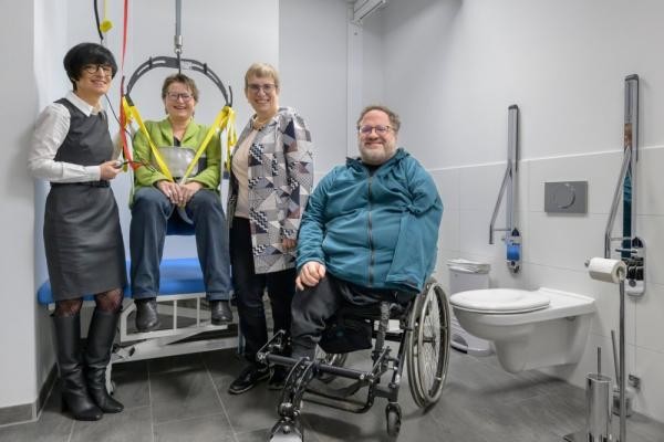 Eine höhenverstellbaren Pflegeliege mit Lifter für Erwachsene gehört zur Ausstattung der „Toilette für alle“. Das Foto zeigt von links beim Test des Lifters: Bürgermeisterin Stefanie Jansen, die Behindertenbeauftragte der Stadt Heidelberg Christina Reiß, die Geschäftsführerin des Landesverbands der Körper- und Mehrfachbehinderten (LVKM) Jutta Pagel-Steidl sowie den Vorsitzenden des Beirats von Menschen mit Behinderungen Czeslaus Mandalka.