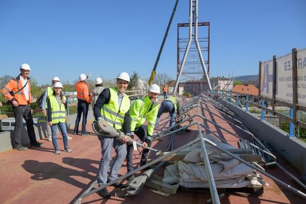 Zwei Männer in Baustellenkleidung stehen auf einer Brücke und halten ein Stahlseil in die Hlhe.