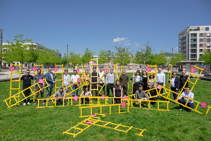 Gelbe Leitern bringen den Einzelhändlern in der Bahnstadt mehr Sichtbarkeit: Auf der Pfaffengrunder Terrasse stellten die Händlerinnen und Händler gemeinsam mit Stadtteilmanagerin Claudia Bitti (stehend, 4. von links) und Marc Massoth (stehend, 3. von links), Leiter des Amtes für Wirtschaftsförderung und Wissenschaft, das neue Projekt vor. (Foto: Philipp Rothe) Größere Menschengruppe posiert mit einigen gelben Leitern auf einer grünen Wiese.