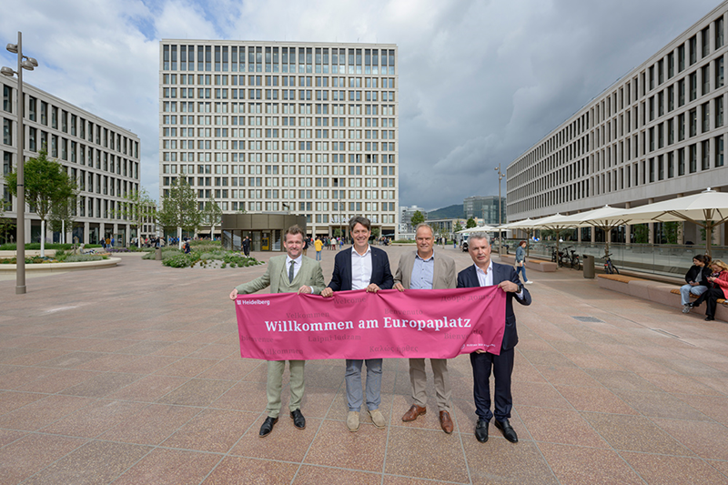 Ein Tag, der mit Sehnsucht erwartet wurde – am Freitag, 13. September 2024, fand die offizielle Eröffnung des Europaplatzes statt mit (von links) Bürgermeister Raoul Schmidt-Lamontain, Erster Bürgermeister Jürgen Odszuck, Oberbürgermeister Eckart Würzner und Kai. M. Dreesbeimdiek von der Gustav Zech Stiftung. (Foto: Philipp Rothe) Vier Männer in Anzug halten ein heidelbeerfarbenes Banner mit der Aufschrift "Willkommen am Europaplatz"