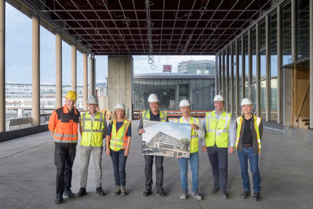 Zentraler Bestandteil des neuen Europaplatzes ist ein Säulengang, der den Europaplatz über eine barrierefreie Fußgängerbrücke mit dem Hauptbahnhof (im Hintergrund) verbindet. Von links: Dr. Ernst Baader (Leiter Landschafts- und Forstamt), Gerald Dietz (Leiter Geschäftsstelle Bahnstadt), Andrea Krastel (Landschafts- und Forstamt), Oberbürgermeister Prof. Dr. Eckart Würzner, Kai M. Dreesbeimdiek (Geschäftsführer Gustav Zech Stiftung), Stephan Sporer (Direktor ATLANTIC Hotel), Volker Schwarz (Landschafts- und Forstamt) bei einer Baustellenbesichtigung im Oktober 2022. (Foto: Philipp Rothe) Eine Gruppe von Menschen mit gelben Warnwesten